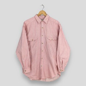 May include: A red and white striped button-down shirt with long sleeves and two chest pockets. The shirt is hanging on a wooden hanger against a light gray background. The shirt has a classic, casual style.