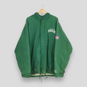 Op de afbeelding: Groene jas met capuchon met het Philadelphia Eagles-logo en NFL-patch. De jas heeft een taille met trekkoord, knoopsluitingen en een Starter-logo op de mouw. Hangt aan een houten kleerhanger.