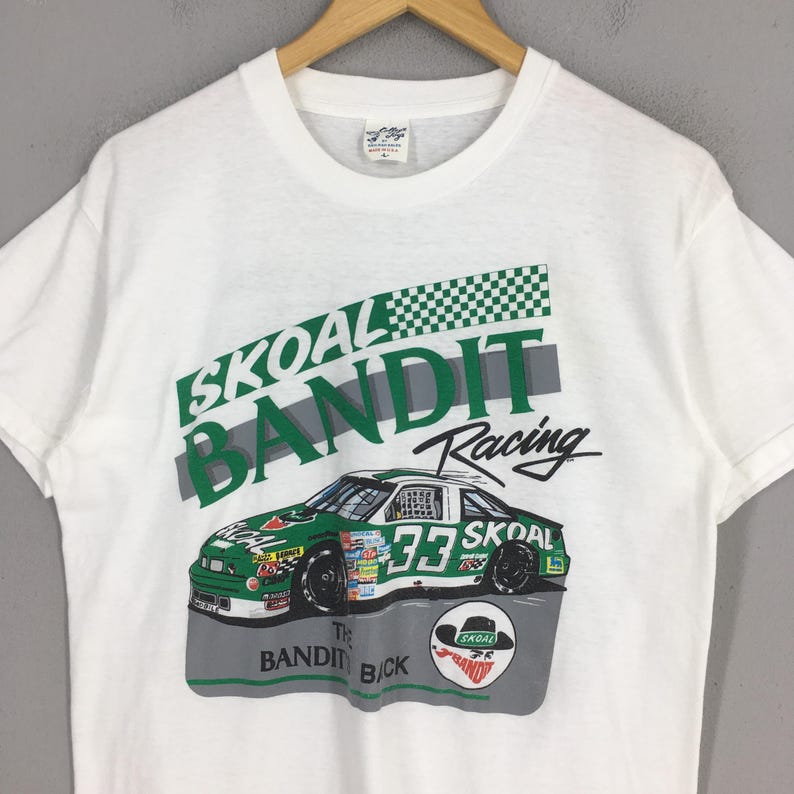 May include: White t-shirt featuring a green and white race car with the number 33, and the words "SKOAL BANDIT Racing". The shirt also has a graphic of a hat and the words "The Bandit Back".