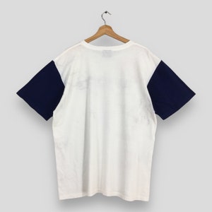 May include: White t-shirt with navy blue sleeves. The shirt has a crew neck and short sleeves.