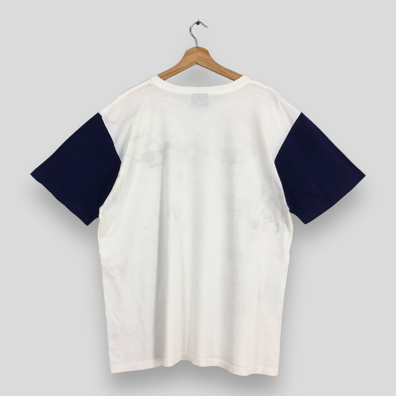 May include: White t-shirt with navy blue sleeves. The shirt has a crew neck and short sleeves.