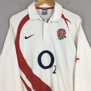 Peut inclure: Maillot de rugby blanc &agrave; manches longues avec des d&eacute;tails rouges et un &eacute;cusson de rose. Comprend un logo "O2" bleu marine et le logo Nike. Le maillot a un col et est suspendu &agrave; un cintre en bois.