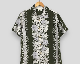 May include: A green short-sleeved shirt with a white floral pattern. The pattern features a repeating design of leaves, flowers, and fruit.
