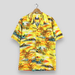 Peut inclure: Chemise jaune à manches courtes avec un imprimé paysage tropical. La chemise présente un motif vibrant de palmiers, de montagnes et d'un coucher de soleil. La chemise est suspendue à un cintre en bois.