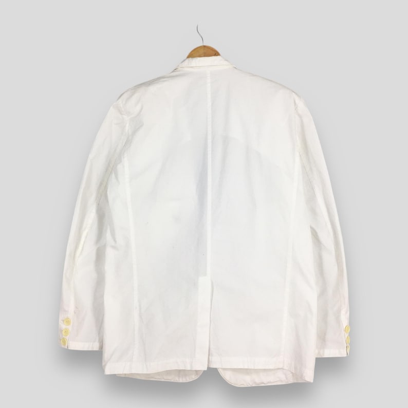 May include: A crisp white blazer featuring a classic notched lapel, long sleeves with three small buttons on each cuff, and a single center back vent. The garment is constructed with visible vertical seam detailing and a structured collar.