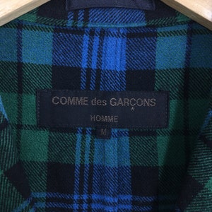 K&ouml;nnte beinhalten: Ein schwarzes und gr&uuml;nes kariertes Hemd mit einem schwarzen Etikett, auf dem "COMME des GARCONS HOMME" und "M" in wei&szlig; steht.