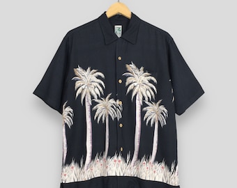 May include: Black short-sleeved button-down shirt featuring a tropical palm tree design. The shirt has a classic collar and wooden buttons. The palm trees are white with pink and brown accents, set against a black background. The bottom of the shirt has a grass and flower design.