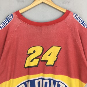 Op de afbeelding: Rode vintage sweatshirt met het nummer 24 in geel. De sweatshirt heeft een gele en blauwe streep aan de onderkant met witte tekst. De mouwen hebben blauwe en witte tekst. De trui hangt aan een houten hanger.