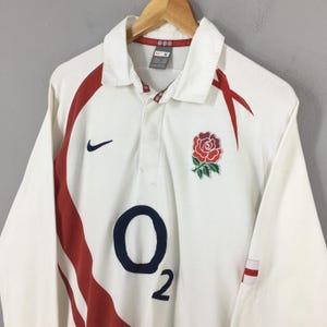 Peut inclure: Maillot de rugby blanc &agrave; manches longues avec des d&eacute;tails rouges et un &eacute;cusson de rose rouge. Comprend le logo Nike et le chiffre 2. Le maillot a un col et est sur un cintre en bois.