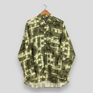 May include: A long-sleeved button-down shirt with a unique pattern. The shirt features a repeating design of olive green and brown shapes and geometric patterns on a light beige background. The shirt is hanging on a wooden hanger.