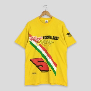 Op de afbeelding: Geel T-shirt met korte mouwen met de tekst "Kellogg's Corn Flakes Racing" en een rode afbeelding van het nummer 5. Het shirt heeft een diagonaal streepontwerp in groen, wit en rood. Een klein logo staat op de mouw.
