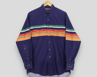 May include: A dark blue button-down shirt with a colorful striped design across the chest and sleeves. The stripes include green, white, orange, and red. The shirt has two chest pockets and buttoned cuffs.