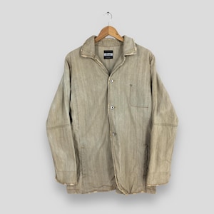 May include: A tan button-up jacket with a collar and a single pocket. The jacket is hanging on a wooden hanger against a light gray background. The jacket has a label that reads "Diesel".