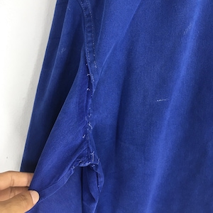 Peut inclure: Gros plan d'une chemise &agrave; manches longues bleu roi. Le tissu montre des signes d'usure, avec des effilochages visibles le long des coutures. La couleur de la chemise est un bleu vif et uni, et la texture du tissu est visible.