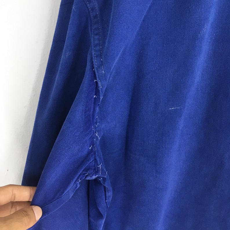 Peut inclure: Gros plan d'une chemise &agrave; manches longues bleu roi. Le tissu montre des signes d'usure, avec des effilochages visibles le long des coutures. La couleur de la chemise est un bleu vif et uni, et la texture du tissu est visible.