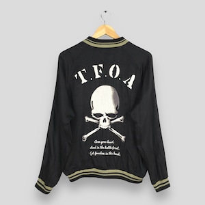 May include: Black bomber jacket with a skull and crossbones graphic on the back. The graphic includes the text "T.F.O.A. Arm your heart, stand in the battle front. Get freedom in this hand."