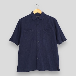 May include: Navy blue short-sleeve shirt with two chest pockets and a button-down front. The shirt is hanging on a wooden hanger. The brand name "NIKO AND..." is visible on the collar.