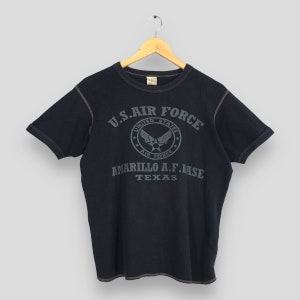 May include: A black t-shirt with a distressed look featuring a vintage-style graphic of the U.S. Air Force logo and the text "U.S. AIR FORCE", "UNITED STATES", "AIR FORCE", "AMARILLO A.F. BASE", and "TEXAS".