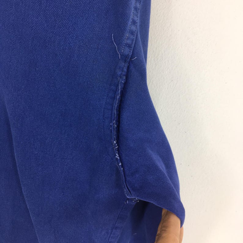 Peut inclure: Gros plan sur une section de tissu bleu, possiblement du denim ou une mati&egrave;re similaire. Le bord du tissu est visible, montrant la couture et les points. Le tissu a un aspect l&eacute;g&egrave;rement textur&eacute;.