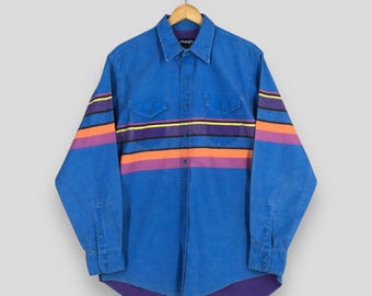 Könnte beinhalten: Blaues Button-Down-Hemd mit horizontalen Streifen in Orange, Lila und Gelb über Brust und Ärmeln. Das Hemd hat zwei Brusttaschen und der Markenname "Wrangler" ist am Kragen sichtbar.