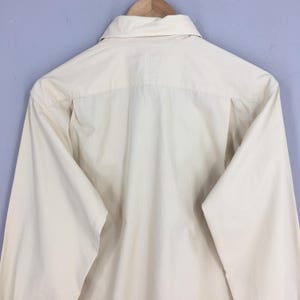 Pode incluir: Uma camisa de bot&otilde;es de manga comprida de cor branca lisa. A camisa &eacute; feita de um tecido leve e tem um caimento cl&aacute;ssico e relaxado.