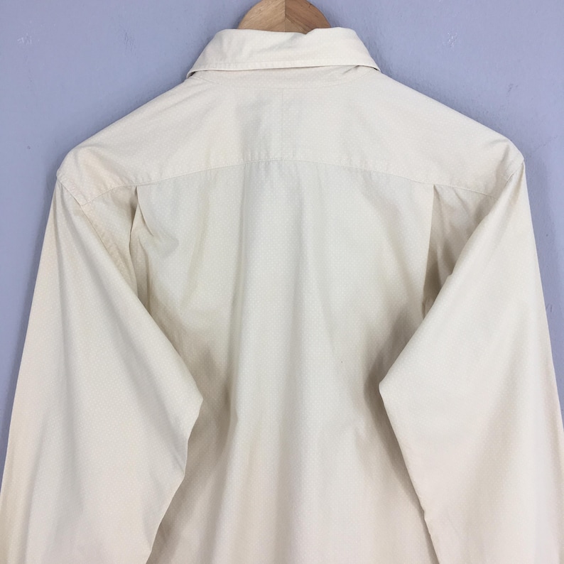 Pode incluir: Uma camisa de bot&otilde;es de manga comprida de cor branca lisa. A camisa &eacute; feita de um tecido leve e tem um caimento cl&aacute;ssico e relaxado.