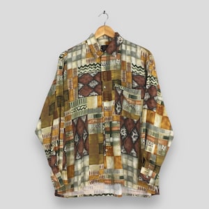 May include: A long-sleeved button-down shirt with a patchwork design in shades of brown, green, and gold. The shirt features a chest pocket and is hanging on a wooden hanger.