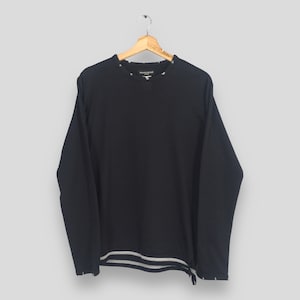 May include: Black long-sleeve shirt with the text "mastermind" on the collar. The shirt has a crew neck and a straight hem. The bottom hem and cuffs have a striped design in white and gray. The shirt is hanging on a wooden hanger.