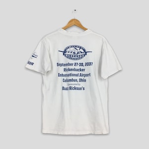 May include: White t-shirt with blue text and graphics. The back of the shirt features the text "Gathering of Mustangs Legends" above the dates "September 27-30, 2007" and location "Rickenbacker International Airport Columbus, Ohio".