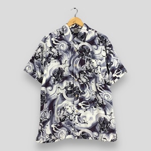 May include: A short-sleeved button-down shirt featuring a repeating graphic print of dark, stylised figures amidst swirling white and grey cloud-like patterns. The shirt has a classic collar, a front button placket, and a single chest pocket.