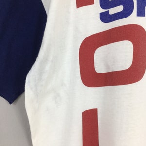 May include: White t-shirt with a blue and red graphic that says "1991" on the front. The shirt has a blue and white color block design on the sleeves.