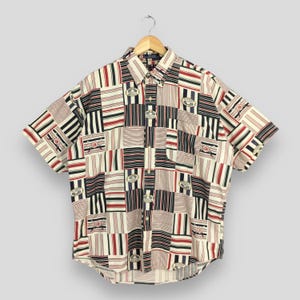 May include: A short-sleeved button-down shirt with a patchwork design. The shirt is made of a white, red, black, and blue patterned fabric.