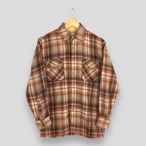 May include: A long-sleeved flannel shirt with a red, brown, and white plaid pattern. The shirt has two chest pockets and a button-up front.