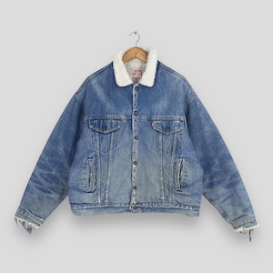 May include: A blue denim jacket featuring a white sherpa collar and lining. The jacket has a button-front closure, two chest pockets with buttoned flaps, and two side pockets. A Levi's brand label is visible on the inside collar area.