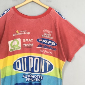 Op de afbeelding: Rood, geel, blauw en groen vintage NASCAR race t-shirt met sponsorlogo's zoals DuPont, Pepsi en Kellogg's. Het shirt heeft de tekst "AUTOMOTIVE FINISHES" en "Jeff Gordon".