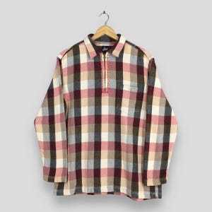 May include: A long-sleeved shirt featuring a plaid pattern in shades of burgundy, beige, white, and grey. The shirt has a collar, a quarter-zip closure with red stitching detail along the zip placket, and a single chest pocket on the left side.