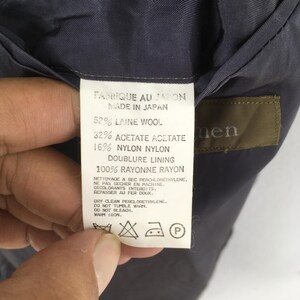 May include: A white garment care label with black text reading Made in Japan, 52% Laine Wool, 32% Acetate, 16% Nylon, and 100% Rayon lining. The label includes care instructions for dry cleaning, no tumble drying, no bleach, and warm iron.