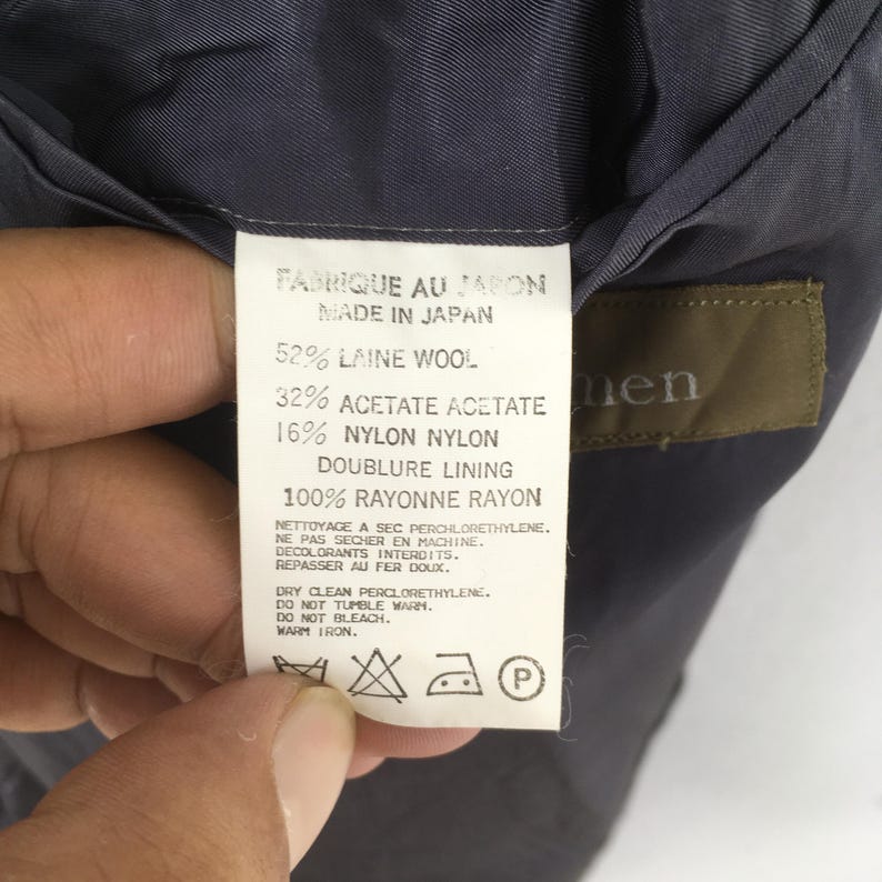 May include: A white garment care label with black text reading Made in Japan, 52% Laine Wool, 32% Acetate, 16% Nylon, and 100% Rayon lining. The label includes care instructions for dry cleaning, no tumble drying, no bleach, and warm iron.