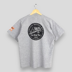 May include: A heather gray t-shirt featuring a circular graphic on the back that reads "Chicago Railroad Fair 100 Years of Railroad Progress 2nd Great Year 1949." The shirt also has a small orange and white patch on the sleeve.