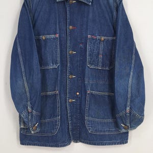 May include: A dark blue denim work jacket with multiple pockets and button closures. The jacket has a classic workwear style and is made of a durable material.
