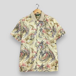 May include: Short-sleeved button-up shirt with a beige collar and a pocket. The shirt features a colorful abstract pattern with shades of yellow, red, purple, and black. It hangs on a wooden hanger against a neutral background.
