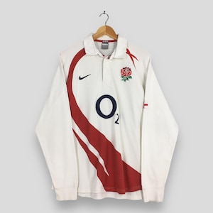 Peut inclure: Maillot de rugby blanc &agrave; manches longues avec des d&eacute;tails rouges et un &eacute;cusson de rose. Comprend un logo "O2" bleu marine et un logo Nike. Le maillot a un col et est suspendu &agrave; un cintre en bois.
