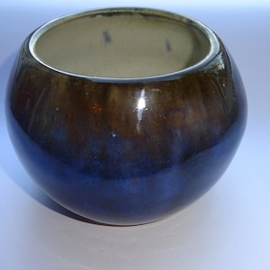 May include: A small, round ceramic bowl with a dark blue glaze and a brown rim. The bowl has a glossy finish.