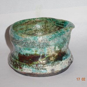 May include: A small, green and white ceramic bowl with a textured surface and a slightly uneven rim. The bowl has a unique, hand-crafted look.