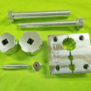 Puede incluir: Un conjunto de herramientas de metal plateado, que incluye dos pernos largos, dos piezas circulares con centros cuadrados marcados con "28" y "32", una pequeña pieza hexagonal, una pieza cilíndrica y una pieza cuadrada con la palabra "GRIP".