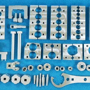 Puede incluir: Un conjunto de herramientas de metal plateado para hacer joyas. El conjunto incluye una variedad de alicates, cortadores y otras herramientas. Las herramientas están dispuestas sobre una superficie azul.