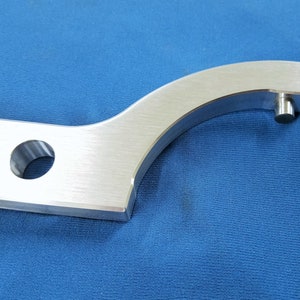 May include: A silver metal wrench with a curved handle and a small hole in the handle. The wrench has a small pin on the end of the handle.