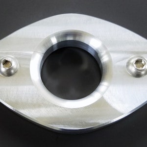 Può includere: Un anello di metallo argentato con un bordo liscio e arrotondato e due piccole viti su entrambi i lati. L'anello ha una superficie testurizzata e un foro al centro.