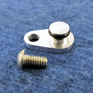 May include: A silver metal part with a round hole and a raised circular section with a black rubber ring. A silver screw with a round head is also shown.