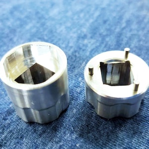 Puede incluir: Dos zócalos de metal plateado con aberturas de diferentes formas. El zócalo de la izquierda tiene una abertura hexagonal y el zócalo de la derecha tiene una abertura cuadrada con tres pequeños pines.